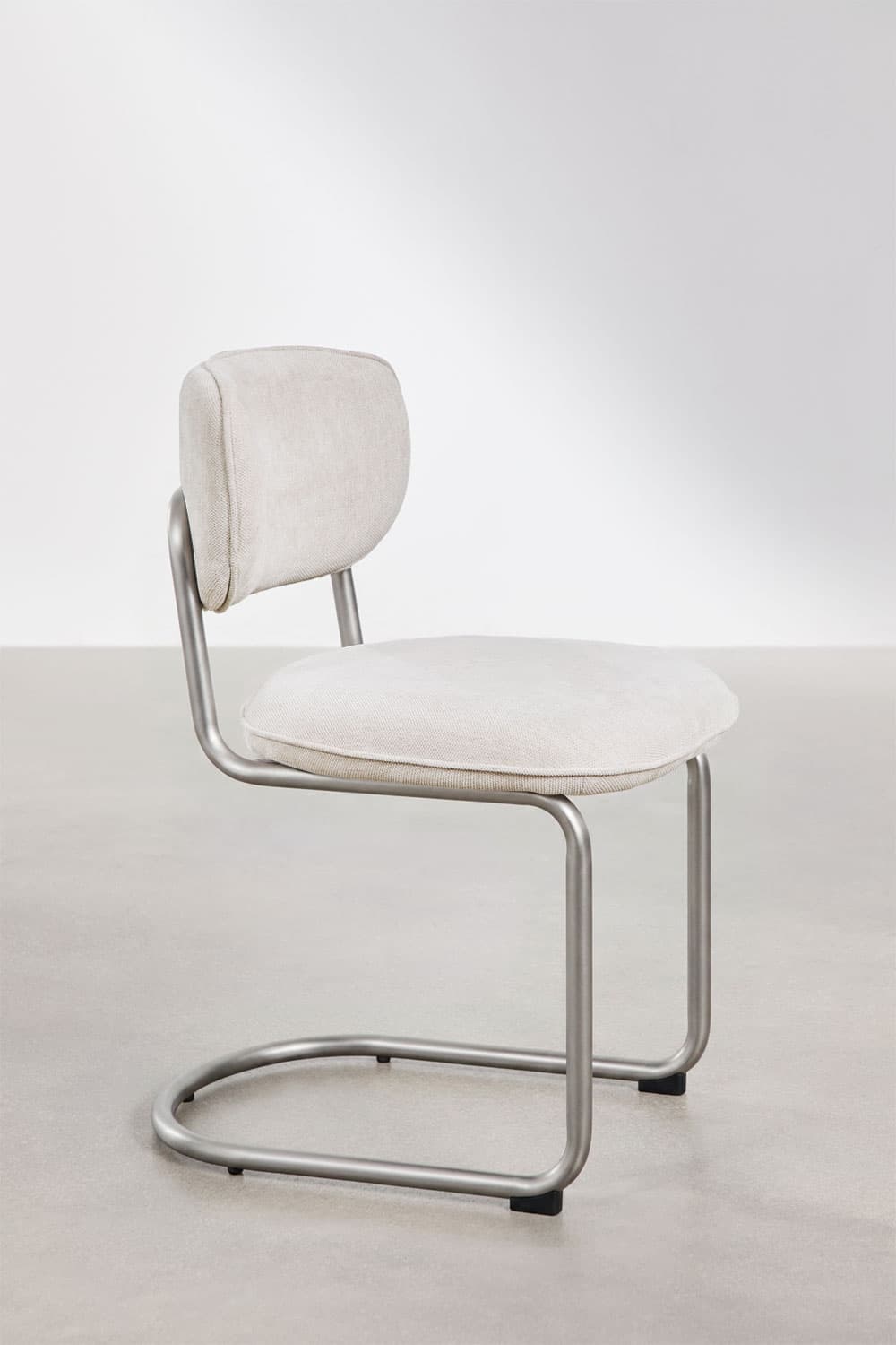 A modern armless chair featuring a bent tubular steel frame in a matte silver finish, with a padded, upholstered seat and a small, separate backrest covered in light-colored fabric. — 3D model