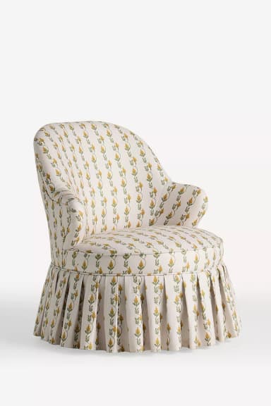 An upholstered armchair with a rounded back, rolled arms, and a pleated skirted base, covered in a cream fabric with a yellow and green botanical pattern. — 3D model