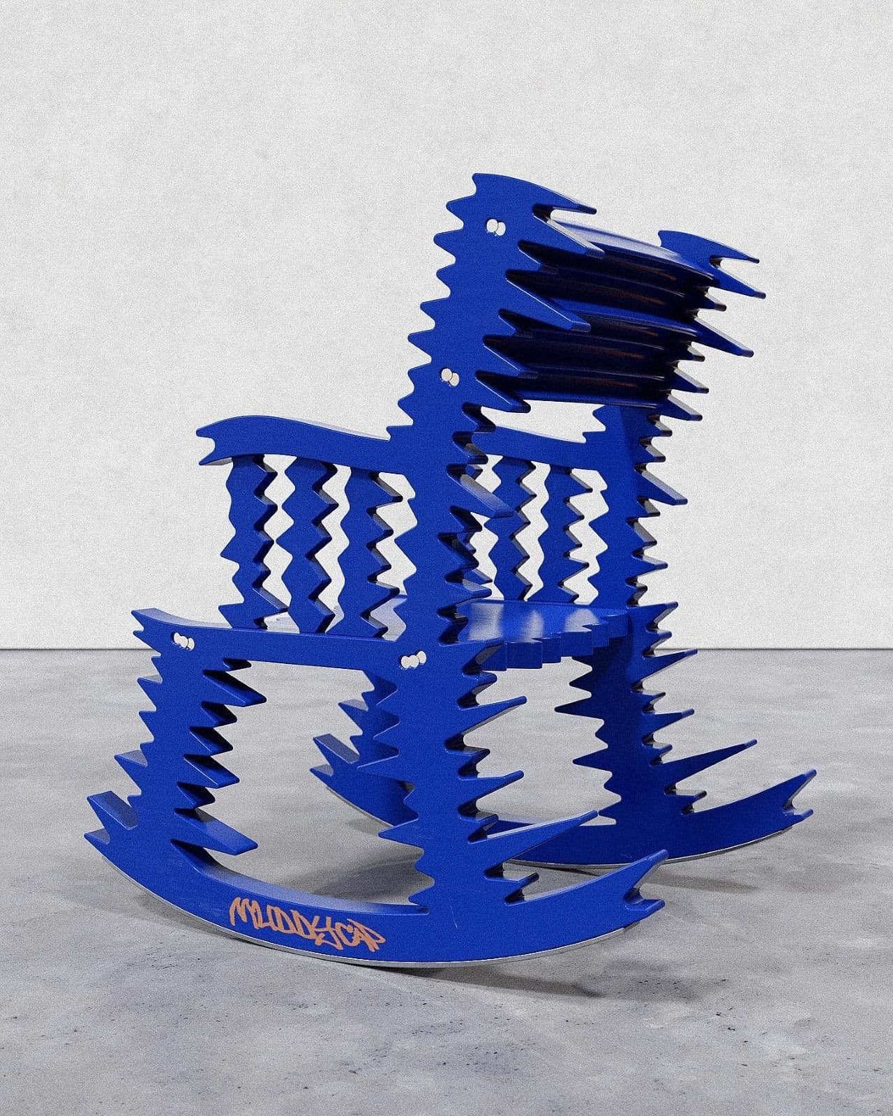 A bright blue rocking chair with a unique, jagged design. The chair features a series of sharp, tooth-like projections along its back, arms, and base. The seat appears to be constructed from layered elements. The rocking base has a distinct curved profile. The chair exhibits a stylized aesthetic, possibly inspired by organic or monstrous forms. There is a visible graffiti-style tag on the left rocking runner. — 3D model