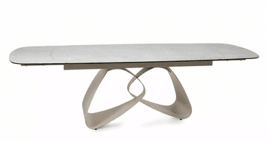 A modern dining table with a rectangular, elongated tabletop featuring softly rounded corners. The tabletop has a subtle texture and appears to be a light, neutral color, possibly white or light gray. It is supported by a sculptural base composed of interlocking, fluid shapes that create an abstract, organic form. The base has a metallic or polished finish, reflecting light and adding a dynamic visual element. The overall design suggests contemporary aesthetics. — 3D model