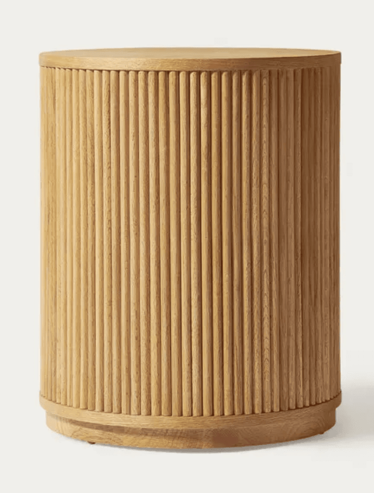 A cylindrical furniture piece made of light-colored wood, featuring a reeded or fluted texture around its entire circumference. It has a flat top surface and a slightly recessed wooden base. The wood grain is visible, indicating a natural finish. — 3D model
