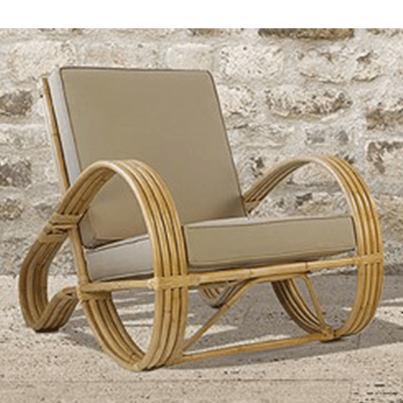 A rattan armchair with curved armrests and circular base supports. The chair features thick cushions for the seat and back. The frame is constructed from multiple rounded rattan poles, creating a distinctive, sculptural design. The backrest is slightly reclined, and the seat appears to be a single cushion. — 3D model