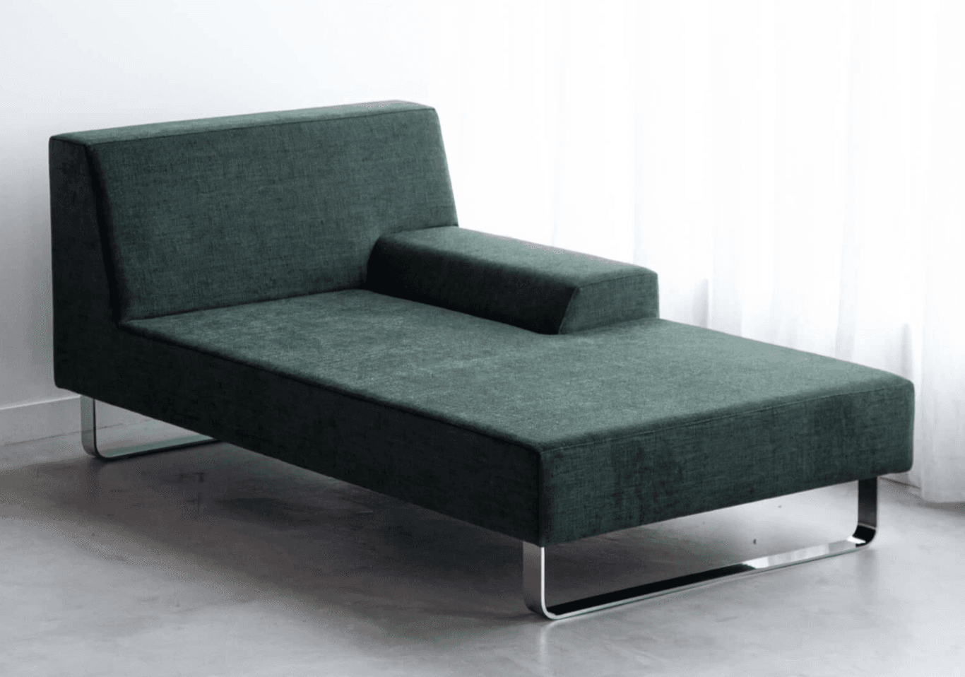 A modern chaise lounge upholstered in a dark green textured fabric. It features a low profile with a rectangular backrest that slopes slightly downwards on one side, and an integrated, elongated armrest on the opposite side. The piece is supported by a minimalist, U-shaped polished metal frame acting as legs. — 3D model