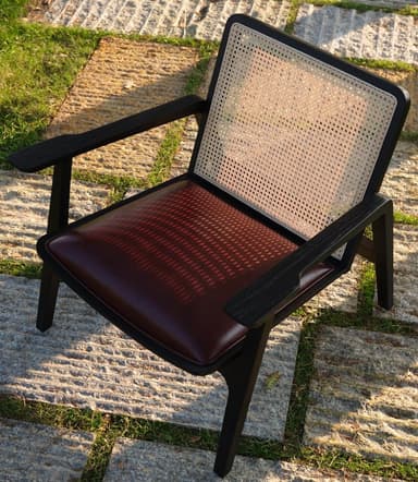 A modern armchair with a dark wood frame and cane back. The seat is upholstered in black material, likely leather or faux leather. The frame has clean lines, with angled legs and armrests. — 3D model