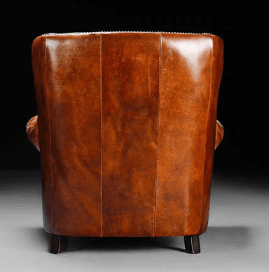 A traditional wingback armchair upholstered in rich, distressed brown leather, featuring prominent wingback sides, rolled arms, and extensive nailhead trim. It includes a loose seat cushion and a loose back cushion, supported by dark turned wooden bun feet. — 3D model