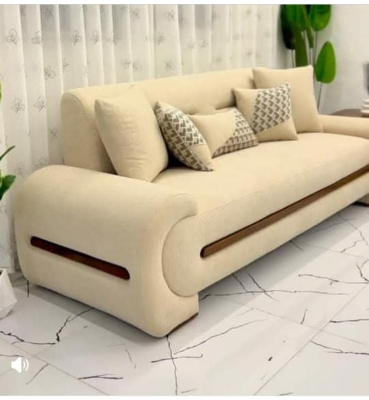 A contemporary three-seater sofa upholstered in a light beige fabric, featuring distinctive rolled and curved arms with integrated dark wood accents. It comes with several throw pillows, some patterned. — 3D model