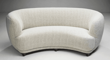 A curved, fully upholstered sofa featuring a serpentine form, rounded back and integrated armrests, and short, tapered wooden legs. It is covered in a light-colored, textured woven fabric. — 3D model