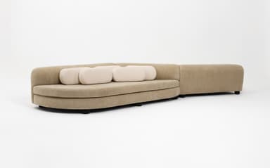 A contemporary sinuous modular sofa featuring a serpentine form, upholstered in a beige textured fabric. The design includes integrated cylindrical backrests/armrests and is accompanied by smaller, contrasting cream-colored cylindrical lumbar pillows. The sofa appears to be composed of two interconnected, curved modules. — 3D model