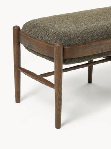 A rectangular upholstered ottoman featuring a solid wooden frame with rounded edges and four tapered legs. The top is generously padded and covered in a textured, greenish-brown fabric, while horizontal wooden stretchers provide structural support. — 3D model