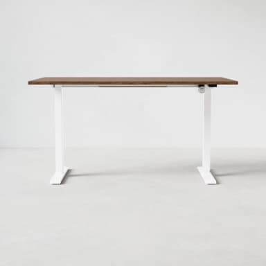 A modern standing desk with a rectangular, wood-grain finished top and white, adjustable legs. The legs have a curved, minimalist design with a flat base for stability. A visible mechanism on the right leg suggests height adjustability. — 3D model