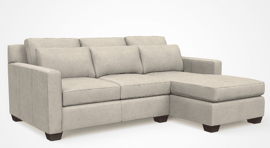 A contemporary sectional sofa featuring a right-facing chaise lounge, upholstered in a light beige or greige textured fabric. The sofa has clean lines, square track arms, and features multiple loose seat and back cushions. It is supported by short, dark, block-style legs, giving it a slightly elevated stance. — 3D model