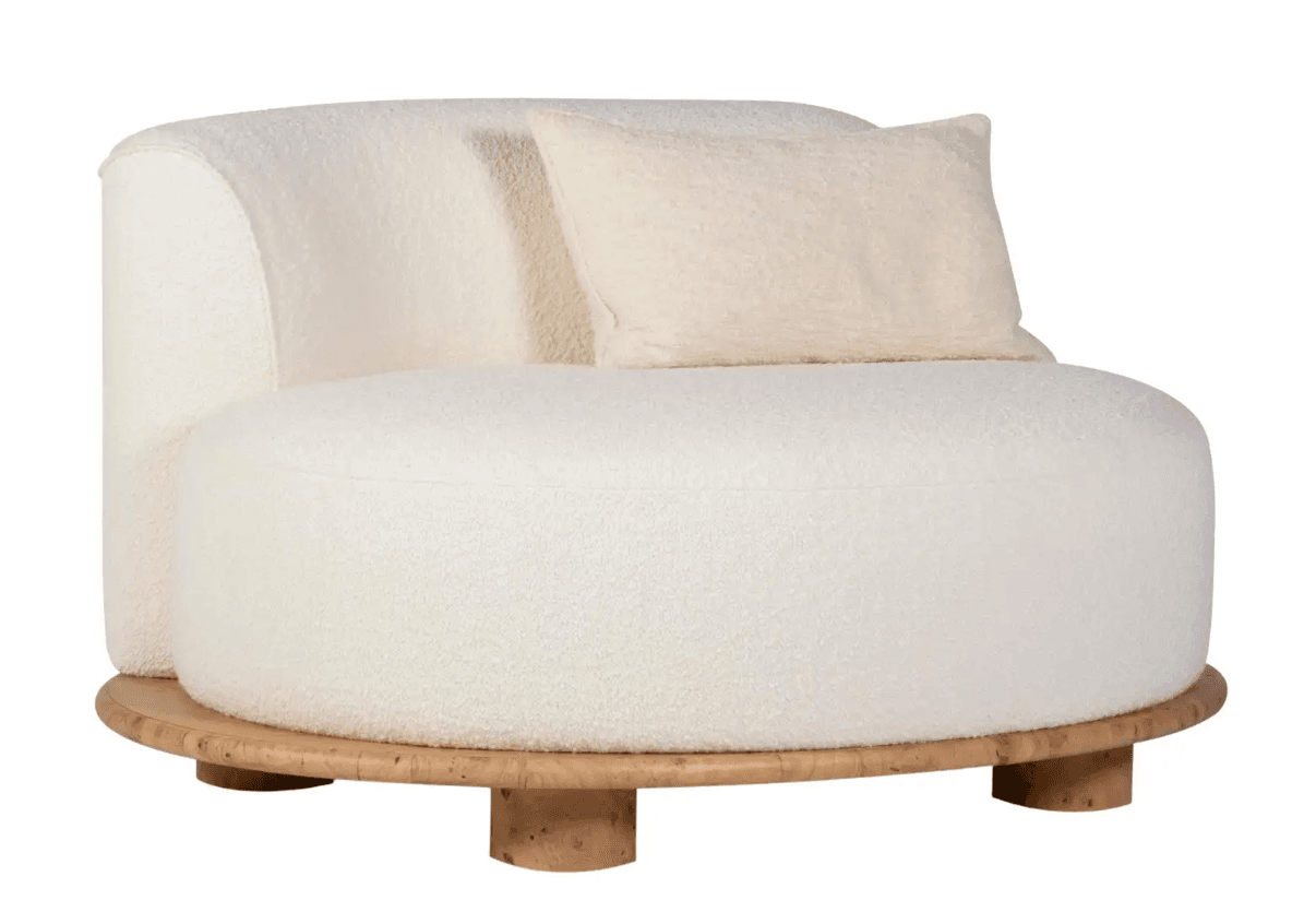 A modern armchair with a rounded silhouette, upholstered in a textured, off-white boucle fabric. It features a low profile with a thick, circular base that transitions into short, cylindrical legs. A single, rectangular throw pillow made of the same boucle fabric is placed on the seat. The base appears to be constructed from a light-colored wood with a visible grain pattern. — 3D model