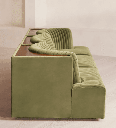 A contemporary sofa upholstered in a rich green velvet, featuring distinctive channel tufting across its backrest and seat. The sofa integrates a continuous wooden surface that serves as armrests and a functional back shelf, with sculpted cut-outs that conform to the upholstered backrest. — 3D model