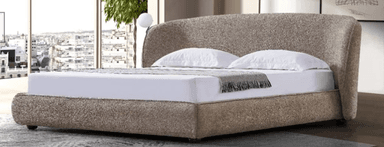 A contemporary upholstered bed with a curved headboard. The bed frame is low-profile and appears to be made of a light-colored fabric. It is dressed with white linens, a grey throw blanket, and decorative pillows. A small, organically shaped side table with a marble-patterned top and a sculptural base is placed to the left of the bed. To the right, a small, dark-colored stool-like side table is visible. A rug with abstract green and beige shapes is partially in view in the foreground. — 3D model