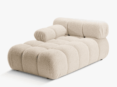 A contemporary chaise lounge featuring an innovative design with multiple rounded, pillow-like upholstered segments. The piece is finished in a light beige or off-white fabric, providing a plush and inviting aesthetic. It integrates a low backrest and a small armrest on one side, contributing to its modular appearance and ergonomic comfort. The chaise rests on discreet, low-profile feet. — 3D model