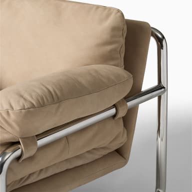 A modern armchair with a tubular chrome frame and plush, upholstered cushions in a camel or mustard yellow hue. The armchair features a low profile and a minimalist design, with the cushions appearing overstuffed and soft. The frame has a distinct cantilevered appearance. — 3D model
