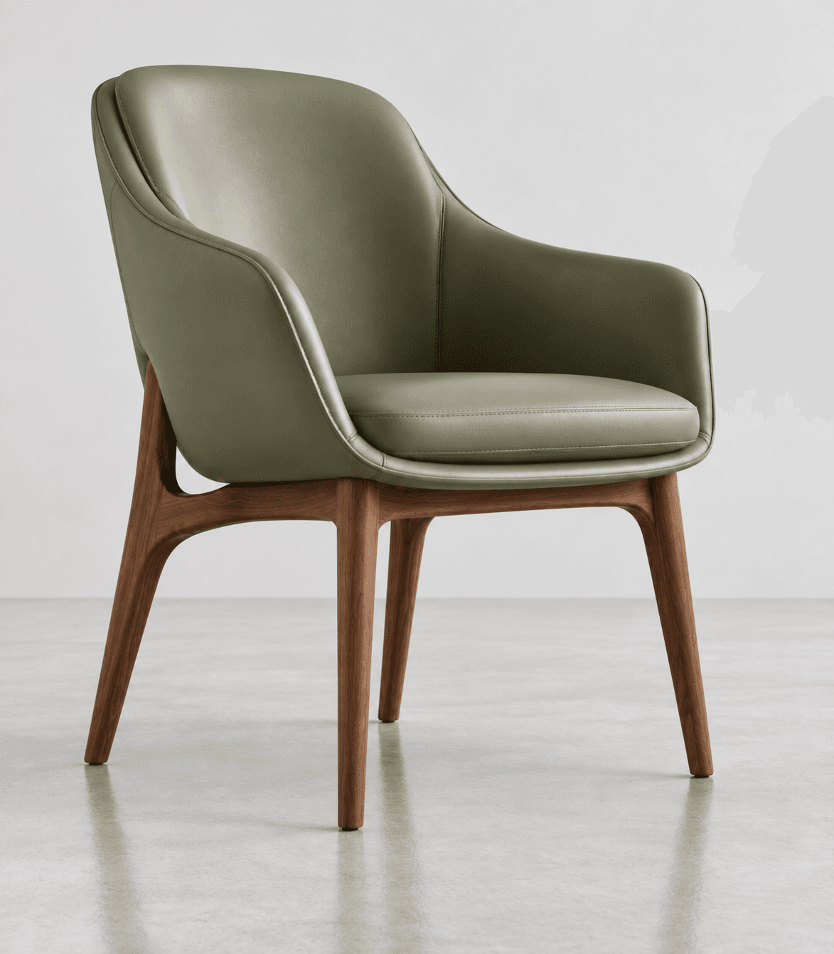 A contemporary armchair featuring a curved, enveloping shell upholstered in a sage green material, likely leather or high-quality faux leather. The chair rests on a splayed and tapered wooden base, providing a modern and elegant aesthetic. It includes a removable seat cushion for added comfort. — 3D model