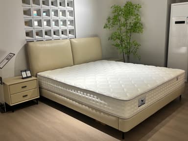 A modern platform bed featuring a low-profile upholstered frame and a distinctive two-panel padded headboard. The bed is presented with a standard white quilted mattress, supported directly by the platform base. The entire frame and headboard are upholstered in a light beige or cream-colored material, and the bed stands on short, tapered black legs, contributing to a clean, contemporary aesthetic. — 3D model