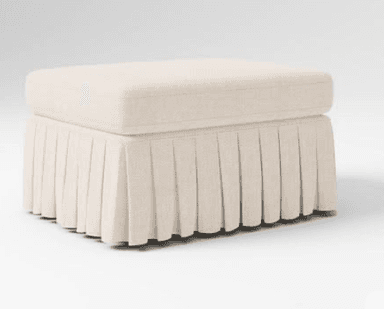 A rectangular upholstered ottoman featuring a padded top cushion and a pleated fabric skirt that conceals its base. The item is rendered in a light, neutral beige fabric with a subtle texture, presented against a clean white background. — 3D model