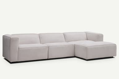 A light beige modular L-shaped sectional sofa with a chaise lounge. The sofa features clean lines, block-style arms, and thick, comfortable cushions. It is upholstered in a textured fabric and rests on discreet, low-profile feet, creating a modern and minimalist aesthetic. — 3D model