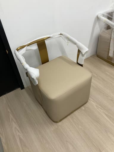 A compact, modern accent chair featuring a square, cream-colored upholstered seat and back. The defining element is a U-shaped brass-toned metal frame that serves as integrated armrests and wraps around to support the low backrest. The chair has a sleek, minimalist aesthetic. — 3D model