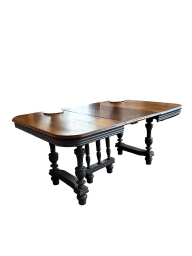 A traditional extendable dining table featuring a polished dark oak tabletop with rounded corners and a dark-stained or ebonized wood base with turned baluster legs and a stretcher system. The table has visible leaves, indicating an extension mechanism. — 3D model