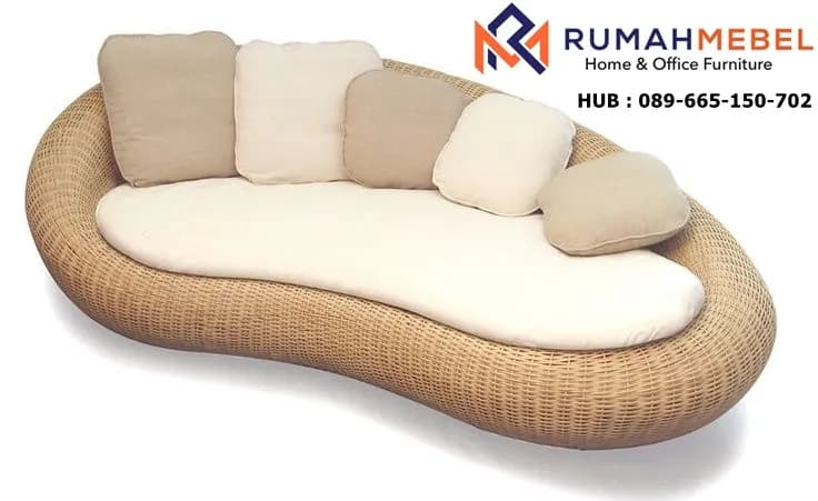 A contemporary outdoor daybed featuring an organic, kidney-bean shape. The base is constructed from woven synthetic rattan or natural wicker in a light brown hue. It is topped with a custom-fitted, off-white or cream-colored mattress, providing a comfortable lounging surface. Several loose throw pillows in complementary beige and cream tones are arranged along one curved edge, serving as a flexible backrest. The design suggests a relaxed, resort-style aesthetic, suitable for outdoor living spaces. — 3D model