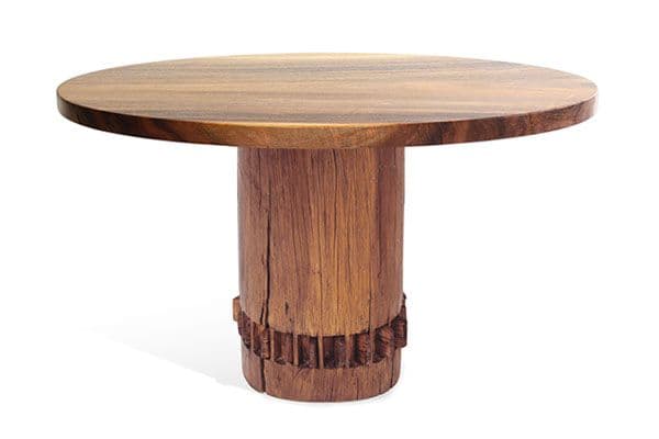 A round dining table constructed entirely from wood, featuring a substantial circular top supported by a thick cylindrical pedestal base. The base has a distinctive carved or grooved detail around its lower circumference, adding textural interest. The wood grain is prominent across all surfaces, suggesting a natural and robust aesthetic. — 3D model