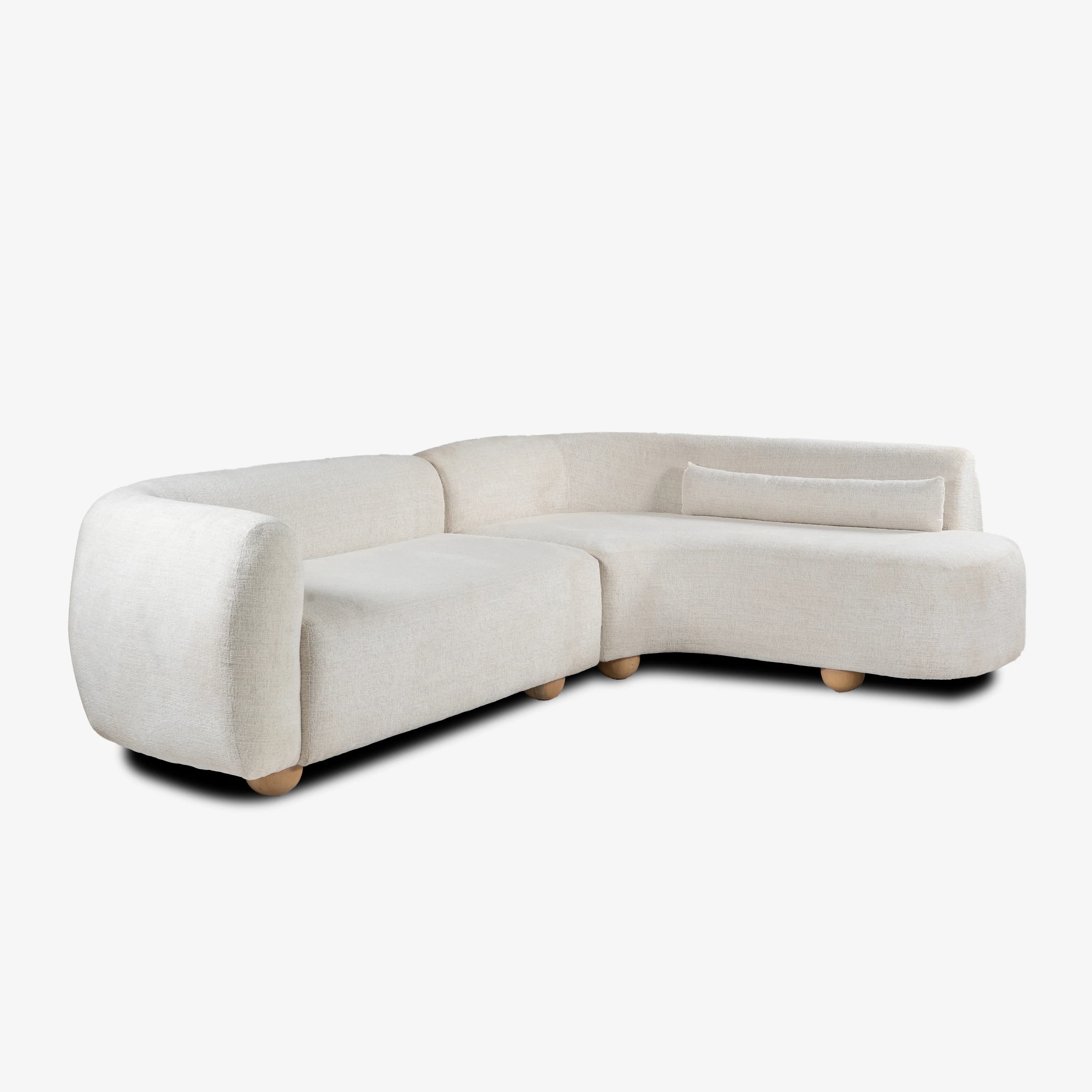 A contemporary L-shaped sectional sofa upholstered in a light cream-colored bouclé fabric. The sofa features a distinctive curved design with rounded armrests and backrests, giving it a soft, organic silhouette. It is supported by small, spherical light-colored wooden feet, visible beneath the fully upholstered base. A matching lumbar pillow is included on the longer section of the sofa. — 3D model