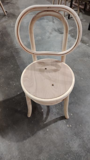 A light-colored wooden side chair with a curved backrest and a circular seat. The chair features bentwood construction, characteristic of classic cafe chairs. It has a simple, elegant design with minimal ornamentation. Two small circular holes are visible on the seat. — 3D model
