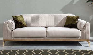 A modern three-seater sofa featuring plush light-colored upholstery, likely cream or off-white, with distinctive channel tufting on the armrests and backrest. The sofa is supported by a sleek, polished brass-finished metal frame that forms the base and extends into four tapered legs. Two olive green throw pillows are included. — 3D model
