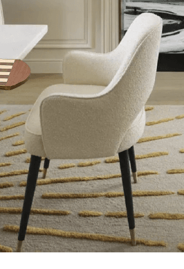 A modern upholstered armchair featuring a curved backrest with a cut-out detail, and an upholstered seat. The chair is supported by four splayed, tapered dark wooden legs, each finished with a brass cap at the foot. The upholstery is a light, textured cream-colored fabric. — 3D model