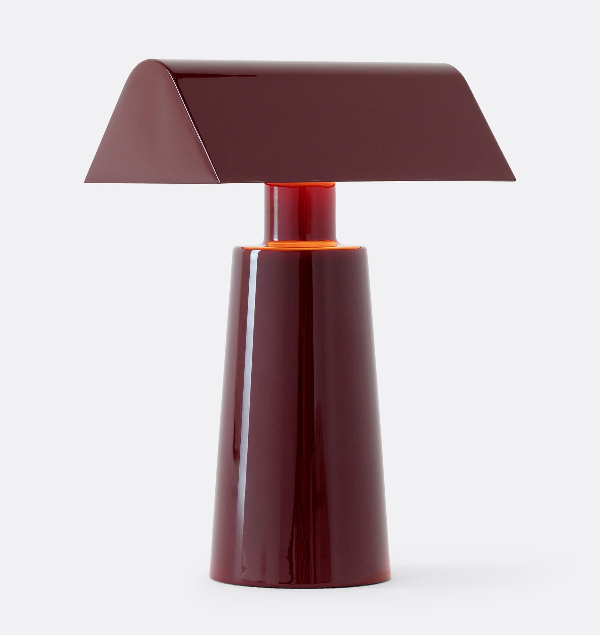 A modern table lamp featuring a distinctive trapezoidal shade and a conical base, both finished in a high-gloss, deep burgundy or maroon color. The shade is rectangular in profile with sloped sides, directing light downwards. The base tapers upwards, narrowing slightly before expanding into a cylindrical neck that connects to the shade. A subtle orange glow is visible at the junction of the base and the shade, suggesting an internal light source or design element. The entire fixture presents a sleek, contemporary aesthetic with a minimalist silhouette. — 3D model