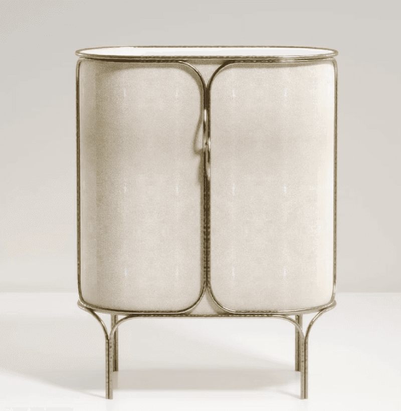 An elegant bar cabinet featuring a rounded rectangular form, clad in a light beige faux shagreen material, and framed by a polished brass-toned metal structure. It stands on slender, tapering legs and has two cabinet doors with integrated pulls. — 3D model