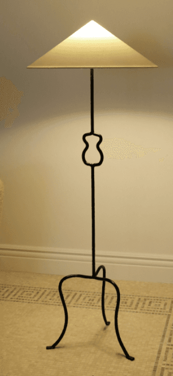 A tall, slender floor lamp featuring a black wrought iron (or similar dark metal) stand and a conical, off-white shade. The stem includes a distinctive curvilinear decorative element in its mid-section. The lamp is supported by a splayed, three-legged tripod base with curved feet. — 3D model