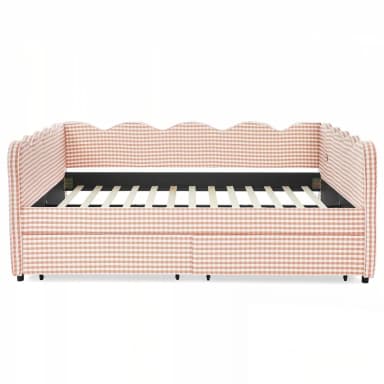 A daybed upholstered in a pink and white gingham fabric with a scalloped headboard and side rails. The frame features a slatted mattress support and appears to have a pull-out trundle bed mechanism beneath the main seating area. Small black feet support the structure. — 3D model