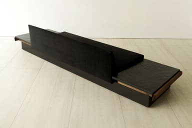 A long, low, contemporary sofa featuring a black velvet upholstered seat and a gently curved backrest, flanked by integrated dark, textured stone side tables, all set within a dark rectangular base with a continuous rounded wooden trim. — 3D model