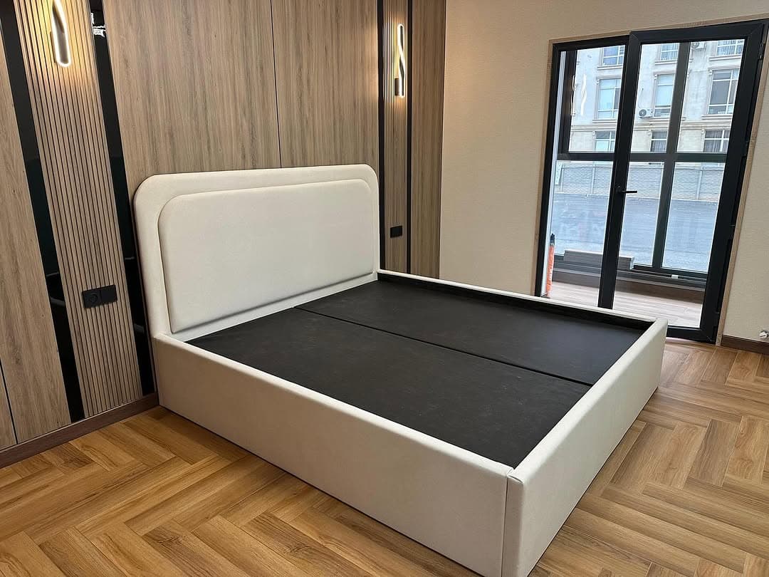 A modern platform bed featuring a light-colored upholstered frame and an integrated headboard with soft, rounded corners, designed to support a mattress without the need for a box spring. — 3D model