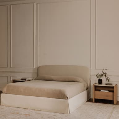 A modern platform bed with a gently curved, upholstered headboard and a rectangular, upholstered base. The bed is dressed in neutral-toned linens. Flanking the bed are two matching wooden nightstands with minimalist designs, featuring drawers and open shelving. — 3D model