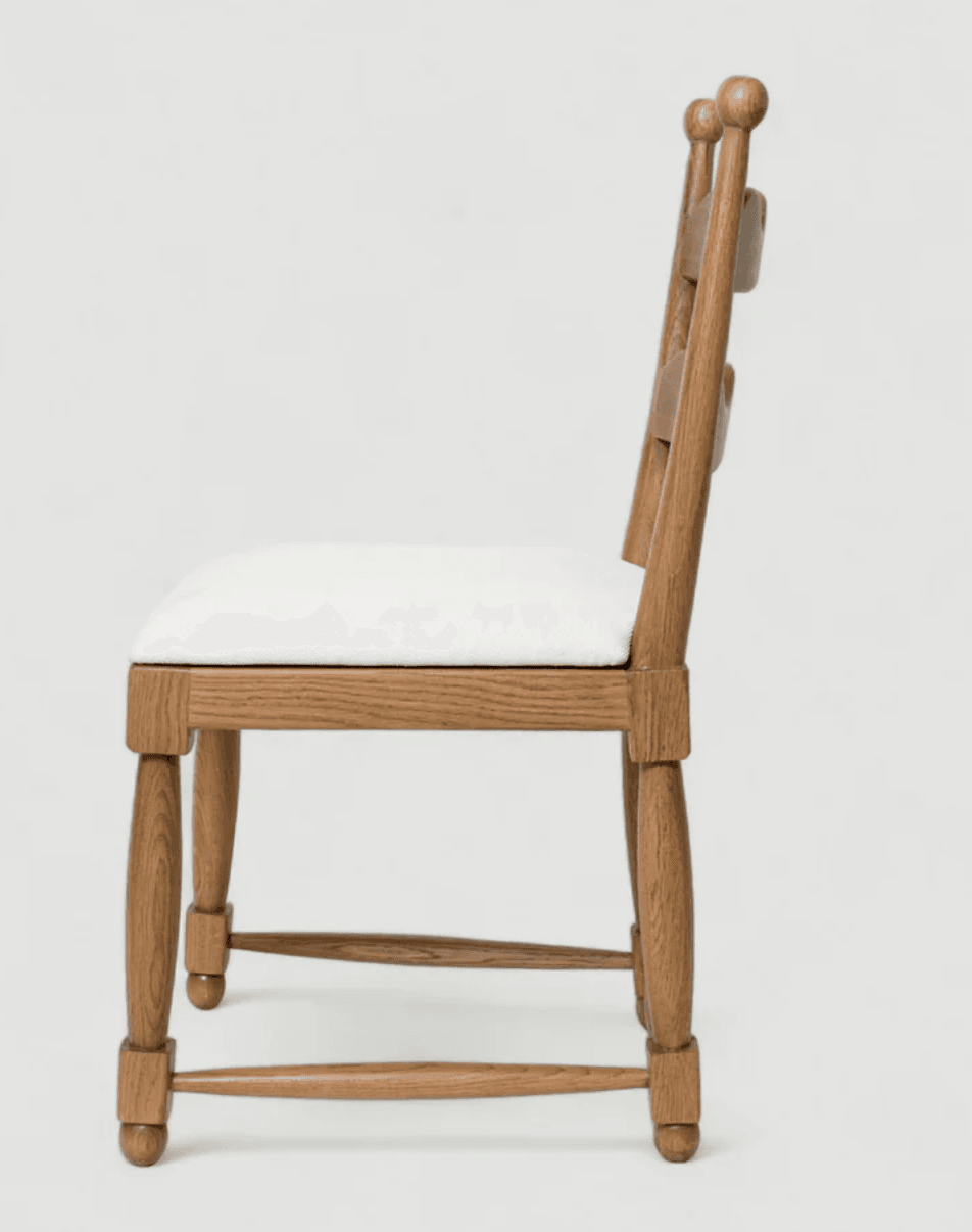 A wooden side chair with a cushioned seat, presented in a side profile against a plain background. The chair features a wooden frame with turned legs and stretchers. The backrest is composed of vertical wooden slats with decorative spherical finials at the top. The seat is upholstered in white fabric. — 3D model