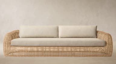 A contemporary sofa featuring a curved, open-weave rattan frame and soft, light-colored upholstered cushions on the seat and back. — 3D model