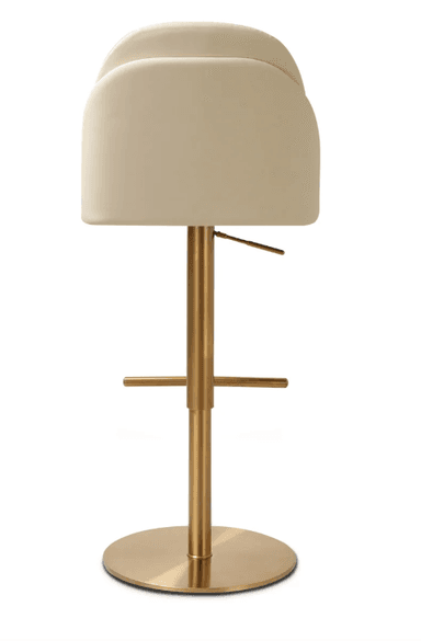 A modern bar stool featuring a cream-colored upholstered seat and backrest, mounted on a brushed brass-finished metallic base. The seat has a rounded, gently curved backrest, offering partial arm support. The central column is height-adjustable via a lever located beneath the seat. A circular footrest extends from the column, and the stool rests on a flat, circular base. — 3D model