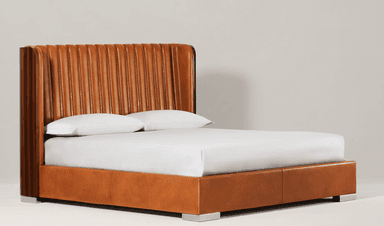 A contemporary platform bed featuring a tall, curved headboard with vertical fluted cognac leather upholstery, flanked by dark wood side panels. The bed frame is also upholstered in matching cognac leather, resting on polished metal block feet. — 3D model