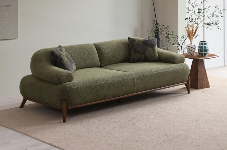 An olive green upholstered two-seater sofa featuring a clean, contemporary design with rounded arms and a continuous backrest. It stands on a dark wooden frame with slender, tapered wooden legs and includes two patterned throw pillows. — 3D model