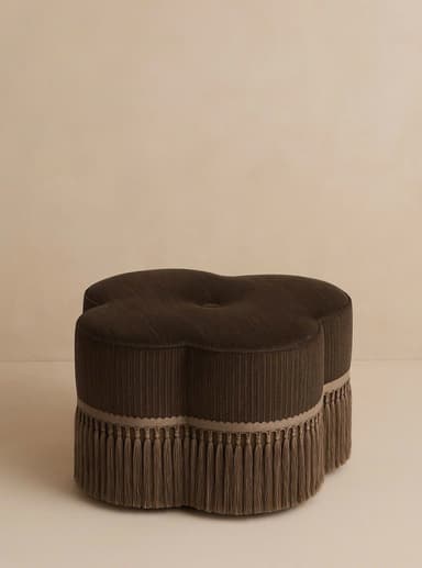 A dark brown, clover-shaped ottoman featuring ribbed upholstery fabric and a decorative fringe trim around its base. A single button tuft is visible on the top surface. — 3D model