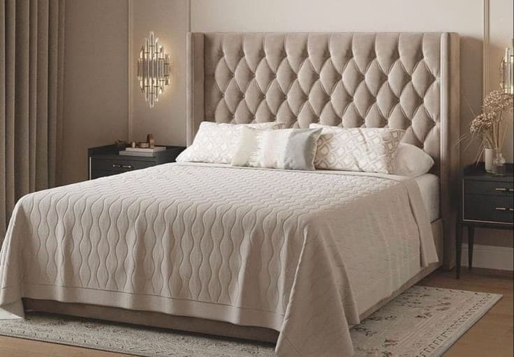 A contemporary upholstered bed featuring a distinctive wingback tufted headboard, rendered in a soft beige or taupe fabric. The headboard showcases deep diamond tufting, creating a luxurious and textured appearance. The bed frame is also upholstered, providing a cohesive and elegant look. The bed is dressed with matching neutral-toned bedding, including a textured bedspread and several decorative pillows. — 3D model