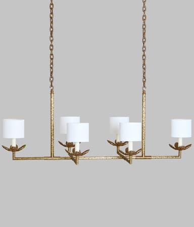 A linear chandelier suspended by two chains. The fixture has a horizontal bar with six lights, each featuring a white cylindrical lampshade supported by a decorative metal arm with leaf-like accents. The metal frame has a distressed gold finish. — 3D model