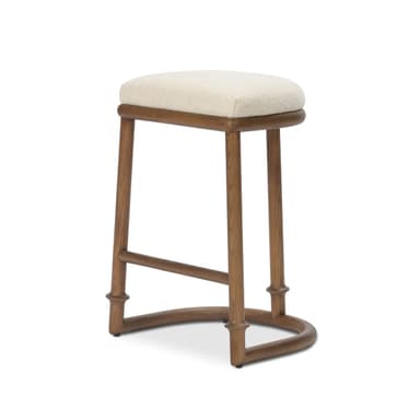 A transitional style bar stool featuring a solid wood frame with a light brown finish and a rectangular, generously padded upholstered seat in a cream-colored, textured fabric. The stool has four subtly tapered legs with decorative turned details near the bottom, connected by a curved, arched footrest for support. — 3D model