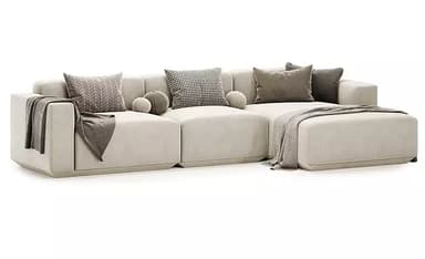 An L-shaped modular sectional sofa in a light beige or off-white upholstery, featuring a low profile, wide track arms, and plush seat and back cushions. The configuration includes a chaise lounge extension on one end. Several throw pillows in neutral tones and varying patterns, along with draped throw blankets, accent the sofa. — 3D model