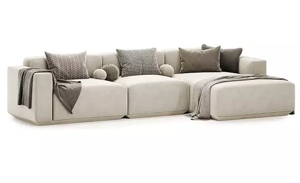 An L-shaped modular sectional sofa in a light beige or off-white upholstery, featuring a low profile, wide track arms, and plush seat and back cushions. The configuration includes a chaise lounge extension on one end. Several throw pillows in neutral tones and varying patterns, along with draped throw blankets, accent the sofa. — 3D model